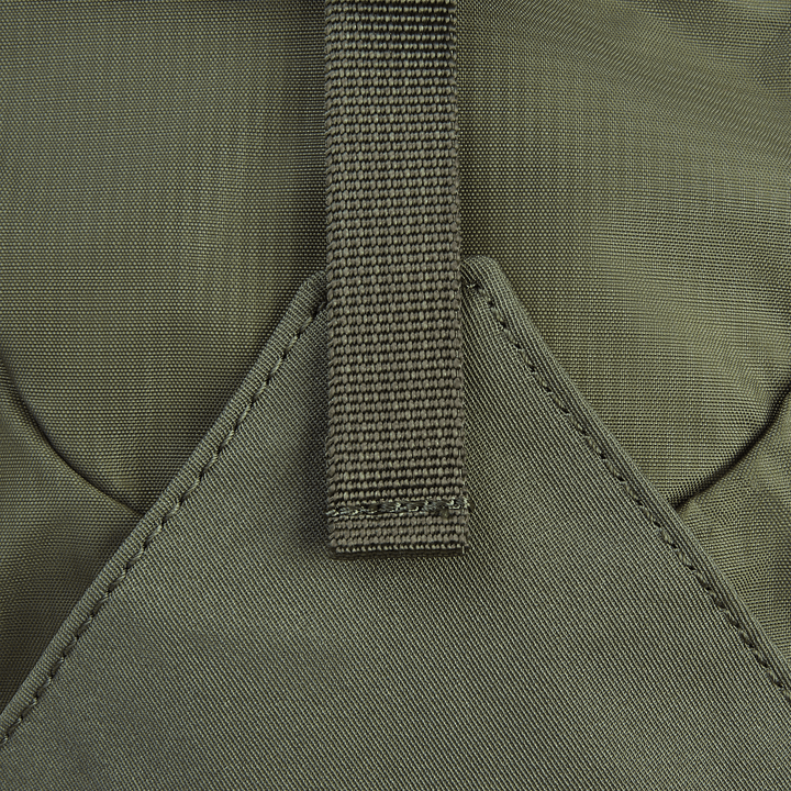 A close-up of the Vertx Long Walks Pack 15L shows a green fabric with Tactigami compatibility, brown strap, and textured pattern on the custom-fit body armor insert. The strap is stitched to a triangular section, with muted colors and durable materials ideal for use.