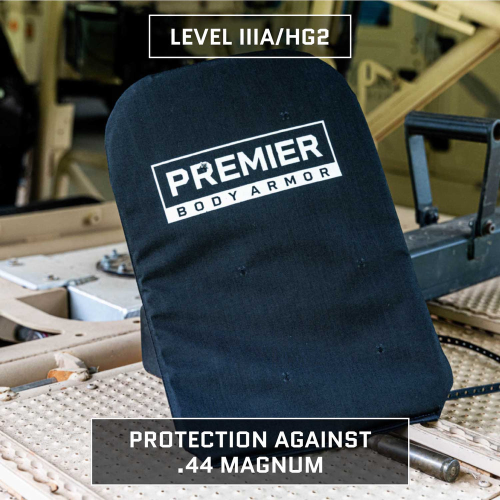 A black Eberlestock Fade Brief Level IIIA Insert by Premier Body Armor is placed on a beige, metallic surface. The text "Protection Against .44 Magnum" is written below the insert, accompanied by an Eberlestock Fade Briefcase. Machinery parts are partially visible in the background.