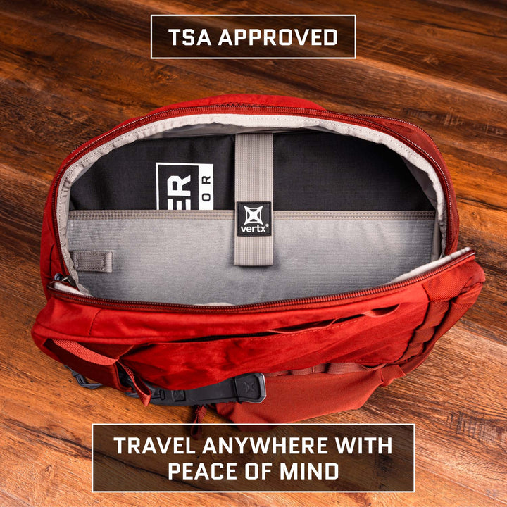 Open red travel bag on wooden floor, showing neat interior pocket with Premier Body Armor 9 x 13.5 Insert Level IIIA Armor (Multicam Black) and gray divider. "TSA Approved" at top, "Travel Anywhere With Peace of Mind" at bottom.