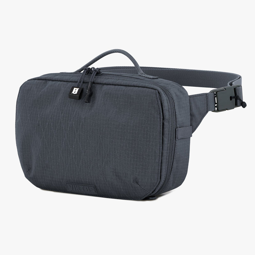 The Viktos Upscale Hip Pack by Viktos/Premier is a gray crossbody bag with textured fabric, a top handle, zipped front compartment, and adjustable buckle strap. Its minimalist design offers space and customization with a custom-fit body armor insert.