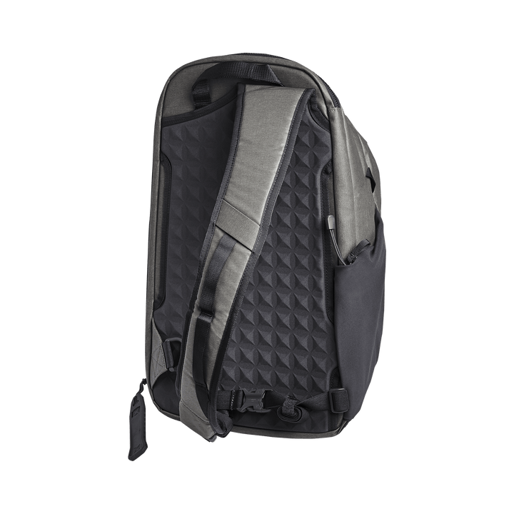 The Vertx Commuter 3.0 Sling backpack in gray and black stands upright against a black background, showcasing its padded straps and textured geometric back panel. It features the Rapid Access Pull design with a zipper pocket and adjustable waist strap on the side.