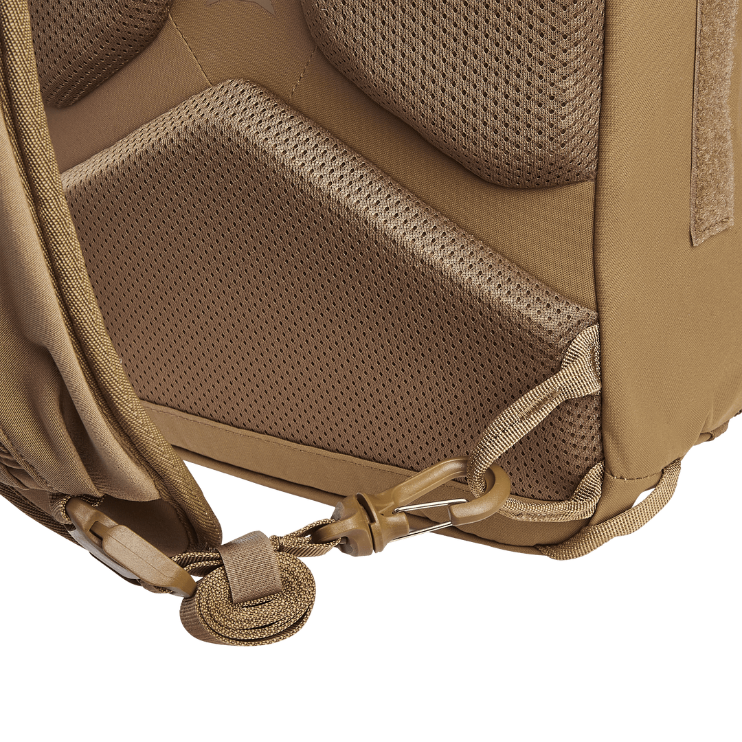 Close-up view of the Vertx Siege 15L Tactical Sling, a brown backpack designed for tactical readiness. It features padded mesh fabric for comfort, a loop and hook system, reinforced stitching, and a discreet CCW compartment against a plain green background.