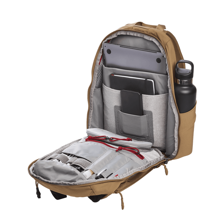 A tan Vertx Siege 15L Tactical Sling is open, showing a laptop, tablet, smartphone, and water bottle. Gray interior pockets and red zipper pulls enhance its design for tactical readiness with multiple compartments for organized storage.