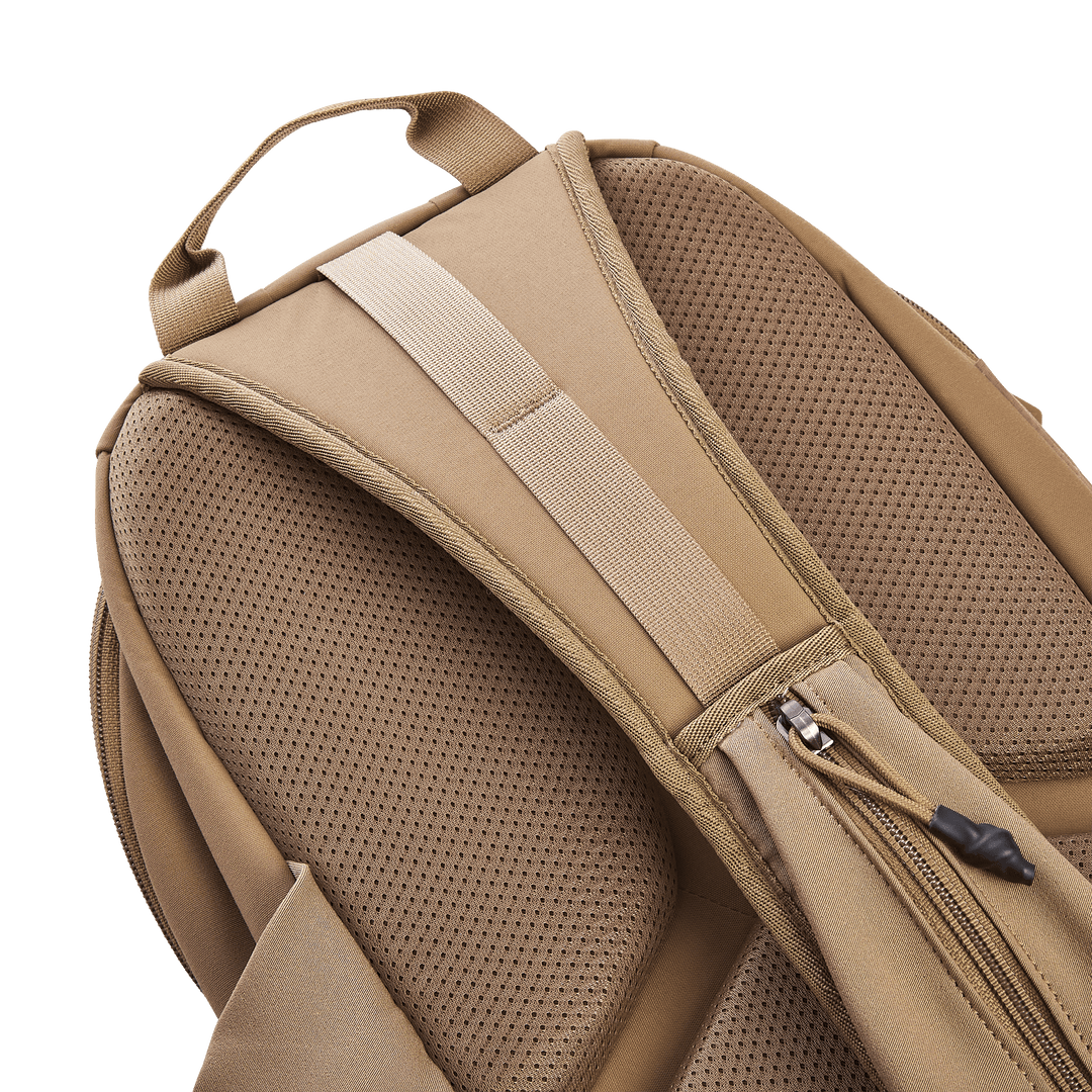 Close-up of a tan Vertx Siege 15L Tactical Sling featuring padded shoulder straps. The mesh-like fabric boosts breathability, and a side zipper pocket adds tactical functionality, combining comfort and practicality for any adventure.