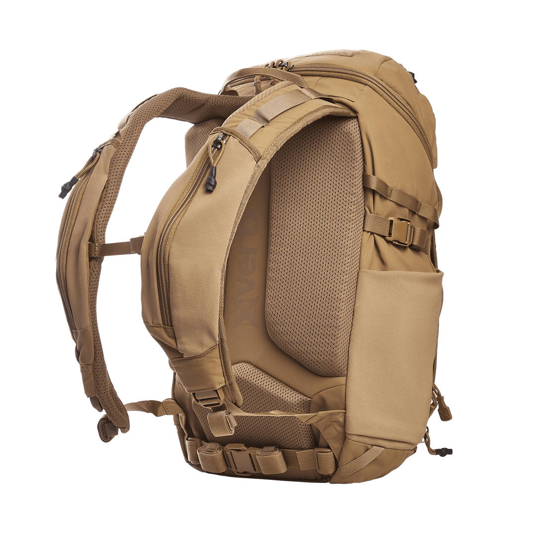 The Vertx Siege 25L Tactical Pack is a tan backpack with versatile functionality, padded shoulder straps, and multiple zippered compartments with buckles. The side view showcases its ergonomic design and textured back panel, highlighting its tactical readiness on a transparent background.