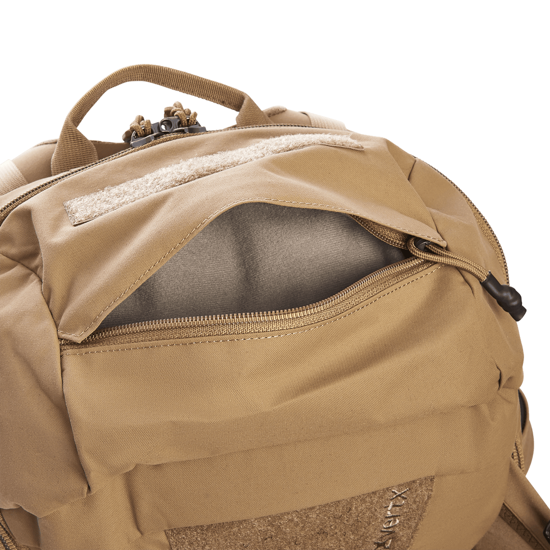 The Vertx Siege 25L Tactical Pack in tan offers versatile use with a partially open front zipper pocket, a light gray interior, padded section, carry handle, and MOLLE webbing for tactical readiness on any adventure.