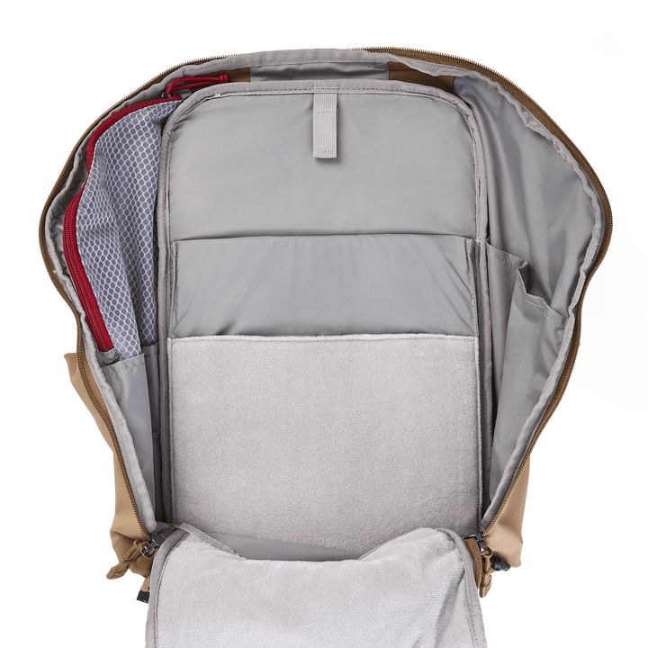 The open Vertx Siege 25L Tactical Pack showcases its tactical readiness with a brown exterior. Inside are multiple compartments, including a large padded laptop section and a mesh pocket with red lining, revealing its versatile functionality and organized layout when fully unzipped.