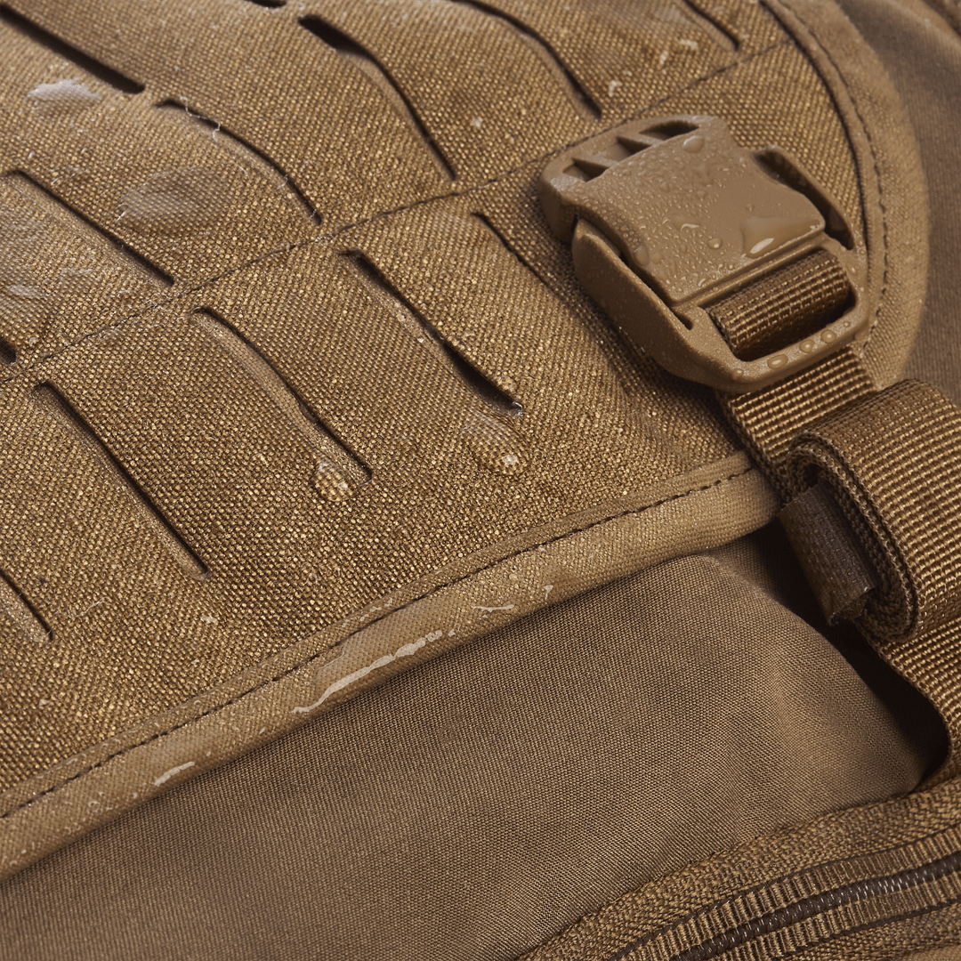 The Vertx Siege 25L Tactical Pack is shown close-up with water droplets on its textured fabric, highlighting its waterproof design. The right-side slot design and plastic buckle enhance its versatile functionality, offering style and tactical readiness.