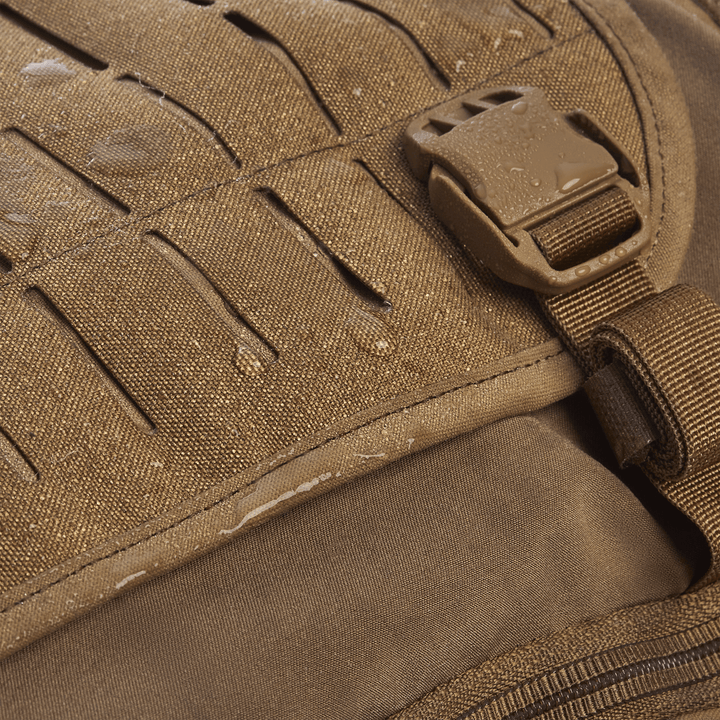 The Vertx Siege 25L Tactical Pack is shown close-up with water droplets on its textured fabric, highlighting its waterproof design. The right-side slot design and plastic buckle enhance its versatile functionality, offering style and tactical readiness.