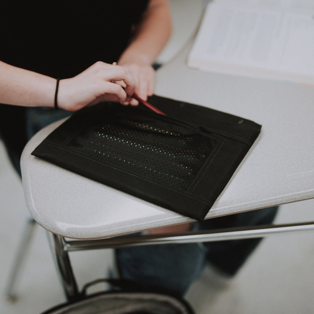 In a light-colored classroom, a person wearing a black shirt opens the Premier Body Armor Level IIIA 3-Ring Pencil Pouch.