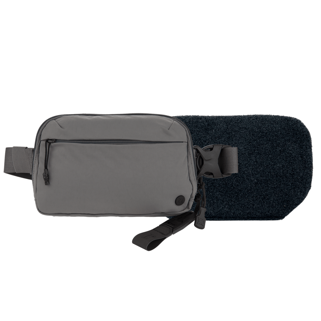 The Armored Vertx Everyday Fanny Pack 2.0 Bundle by Vertx/Premier is a gray rectangular crossbody bag with a zippered front pocket and adjustable black strap, designed to fit an armor insert, shown on a dark textured surface.