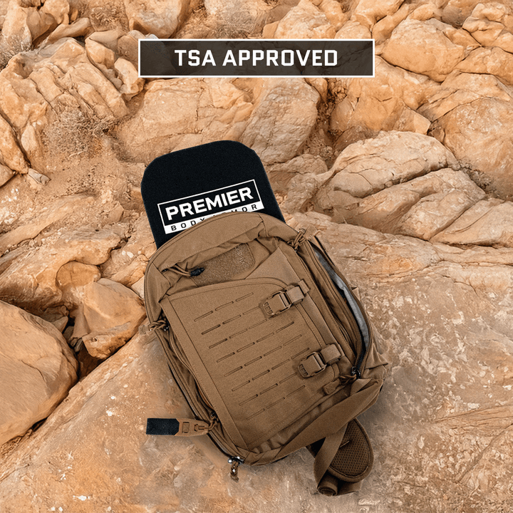 A brown backpack rests on rocky terrain, revealing the "Premier Body Armor" label through its zipper. Offering Level IIIA protection, this TSA-approved Vertx Siege Pack Level IIIA/HG2 Backpack Insert keeps your gear safe and secure anywhere.