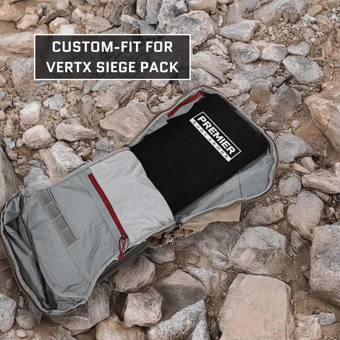 An open gray backpack with red accents lies on rocky ground, showcasing a Level IIIA ballistic insert labeled "Premier Body Armor." This custom-fit, Vertx Siege Pack backpack insert is emphasized by text in the top-left corner.