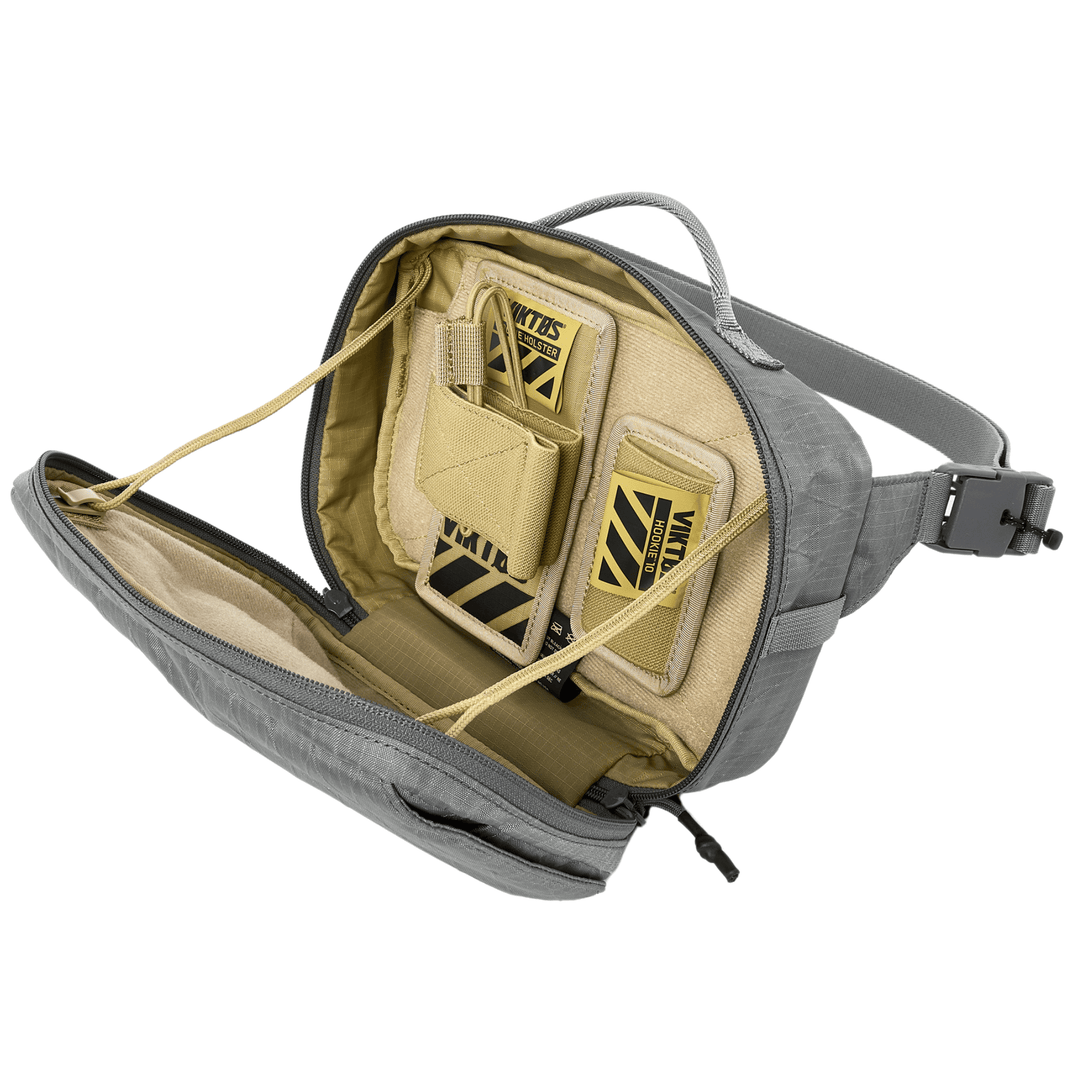 Open the gray Armored Viktos Upscale Hip Pack Bundle by Viktos/Premier to reveal a beige interior with two "Viktos" labeled slots. It features a carry handle, zipper, and adjustable straps, plus compartments with elastic cords and padded sections for concealed carry options.