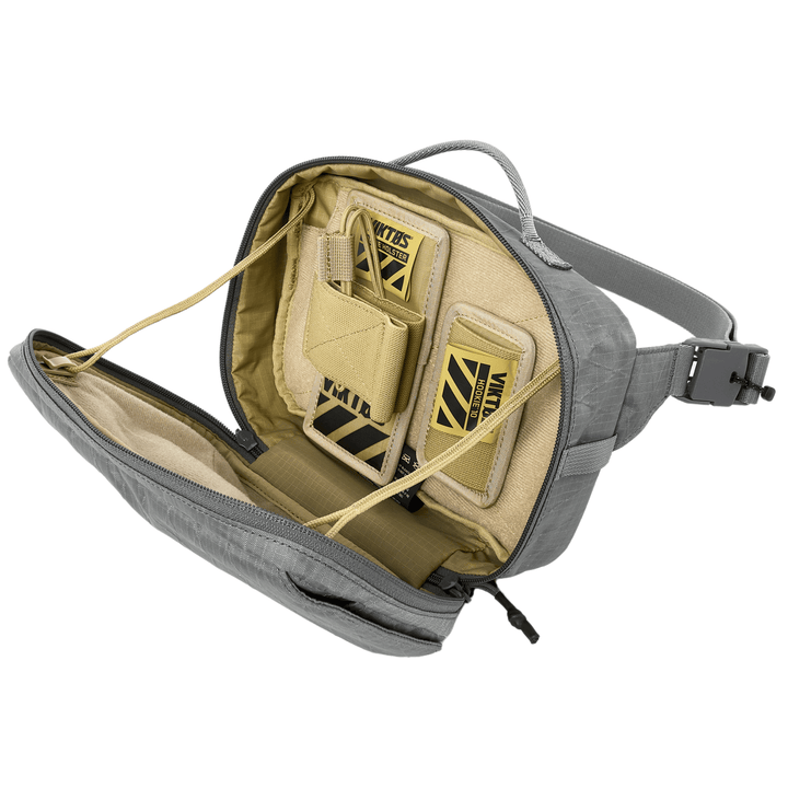 Open the gray Armored Viktos Upscale Hip Pack Bundle by Viktos/Premier to reveal a beige interior with two "Viktos" labeled slots. It features a carry handle, zipper, and adjustable straps, plus compartments with elastic cords and padded sections for concealed carry options.