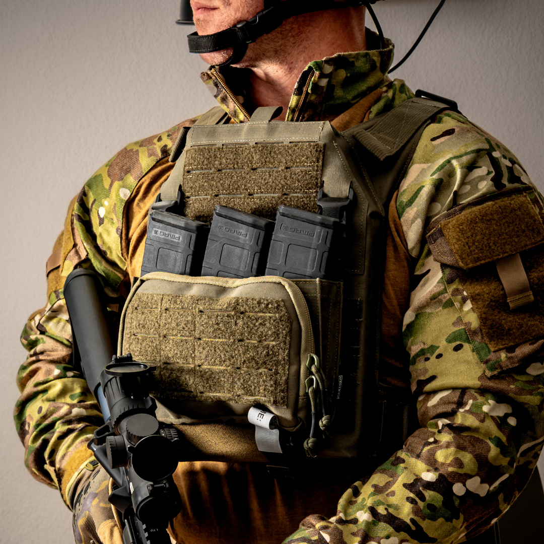 A person in camouflage uniform and tactical gear holds a rifle. Three rifle magazines are in a vest pouch on their chest. Their face is partially out of frame.