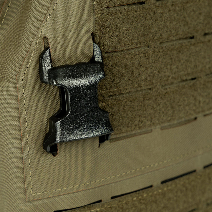 Close-up image of a black plastic buckle attached to a tan 500D Nylon fabric with laser-cut MOLLE slots. The buckle appears to be part of the Premier Body Armor Fortis Alpha Carrier tactical vest. The surrounding fabric has a rugged texture suitable for heavy-duty use.