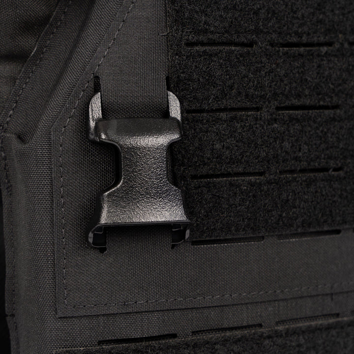 Close-up image of a black plastic buckle attached to textured black fabric, likely part of outdoor or tactical gear. The buckle, featured on the Premier Body Armor Fortis Alpha Carrier, is secured onto a 500D Nylon strap and appears new and in good condition.