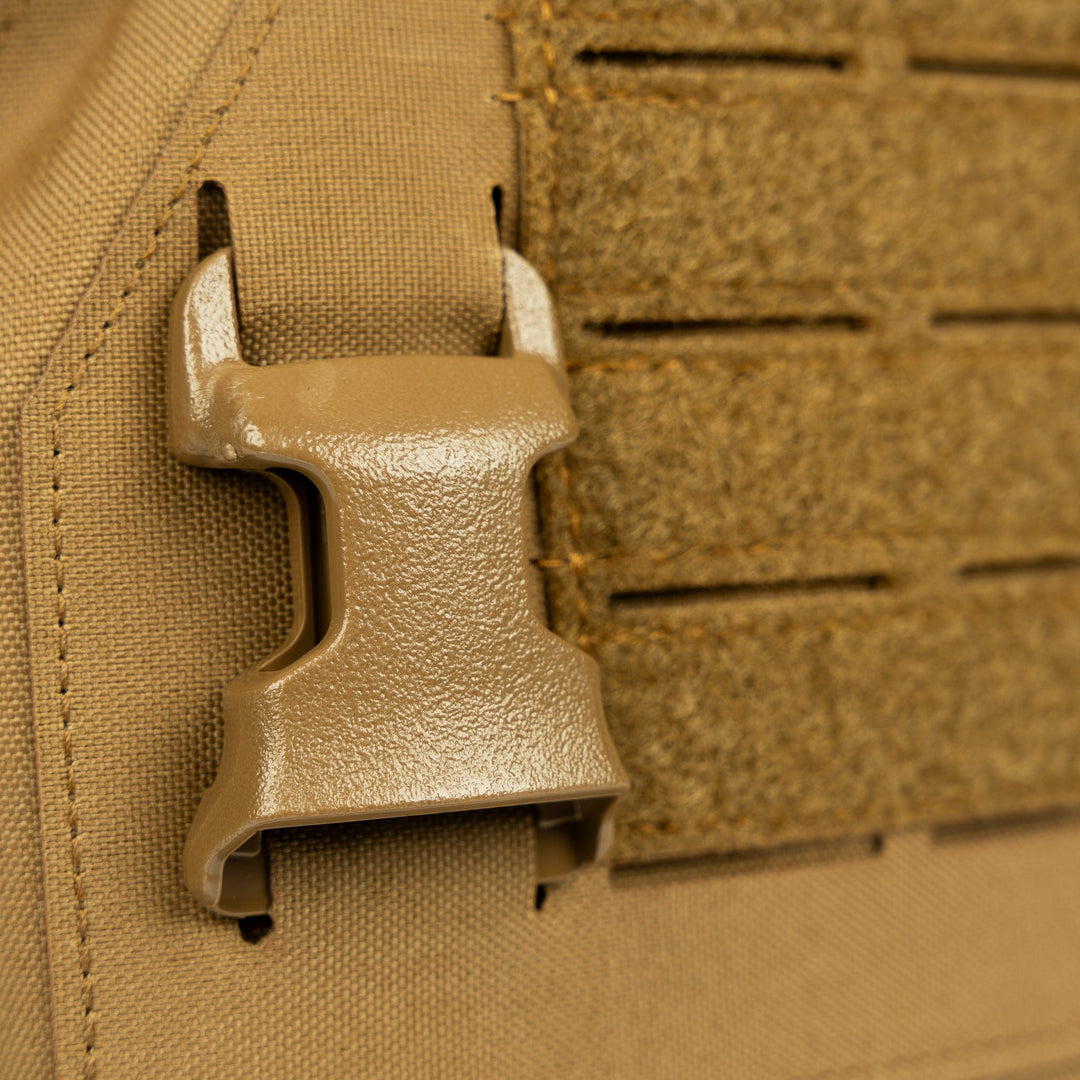 Close-up image of a tan-colored plastic buckle attached to a textured fabric, possibly part of the Fortis Level IV Loadout from Premier Body Armor or similar outdoor gear. The buckle is fastened onto the durable and heavy-duty fabric, which has a Velcro strip beside it, showcasing its tactical flexibility.