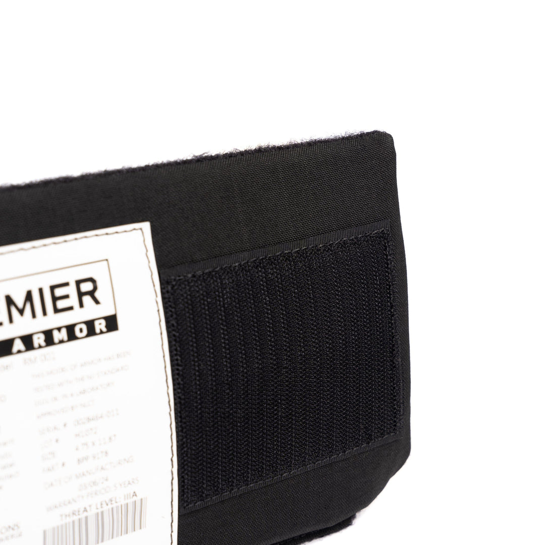 Close-up of a Premier Body Armor product with a visible white label. The black strap and details of the SOE Micro Rig Level IIIA Insert are clearly shown. The label contains text and barcode, but specific details are not readable in the image. Black stitching is visible on the fabric.