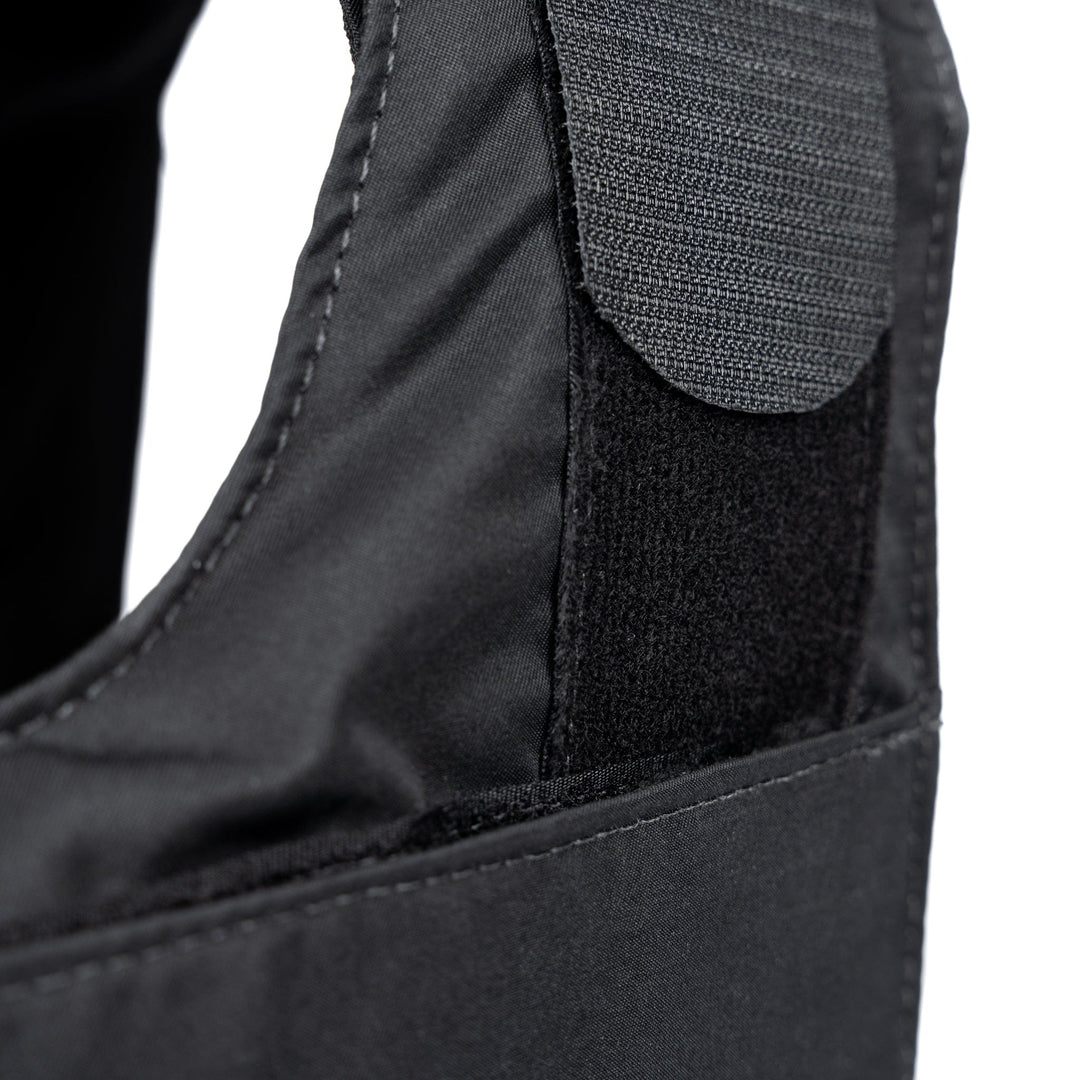 Close-up image of the Overt / Covert Vest Bundle (old) by Premier Body Armor, showcasing a black fabric item with a Velcro patch and strap. The image emphasizes the texture and stitching details, highlighting the vest's durable design ideal for various applications.