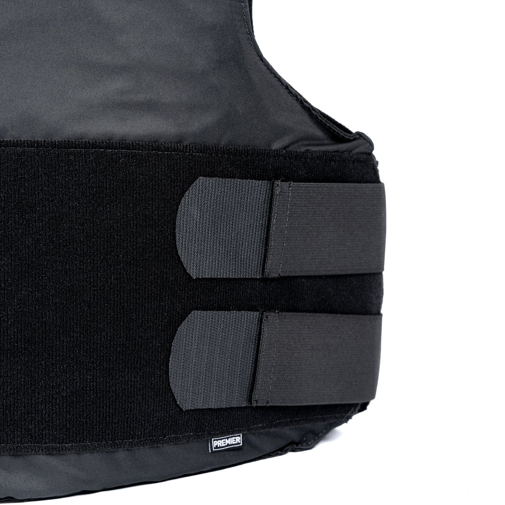 Close-up image of the Overt / Covert Vest Bundle (old) in black, featuring two horizontal Velcro straps for adjustment. The bottom of the vest displays a small label with the text "Premier Body Armor." The background is white.