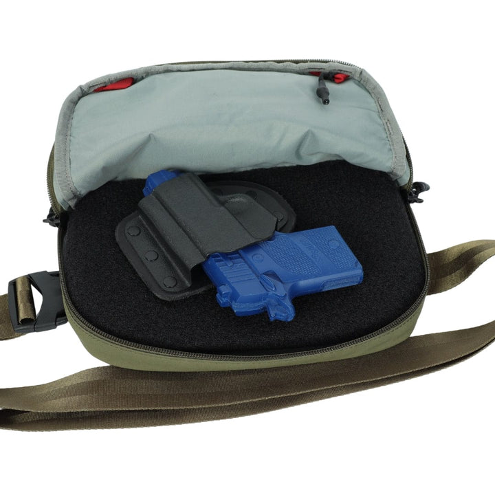 An open green and gray shoulder bag displays a foam insert with a blue training pistol in a black holster, compatible with the Premier Body Armor Vertx Everyday Fanny Pack+ Level IIIA Insert. The bag shows a visible zipper and brown strap.