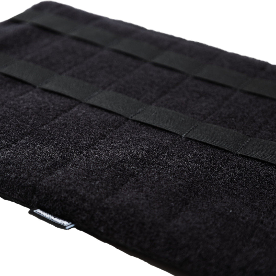 A black rectangular padded organizer mat with grid-like stitching and horizontal straps, lying flat on a white surface. The bottom edge shows a small tag with white text. This versatile mat can be easily integrated into your Premier Body Armor Fieldcraft Survival Small Mobility Level IIIA Bag Insert for effortless organization on the go.