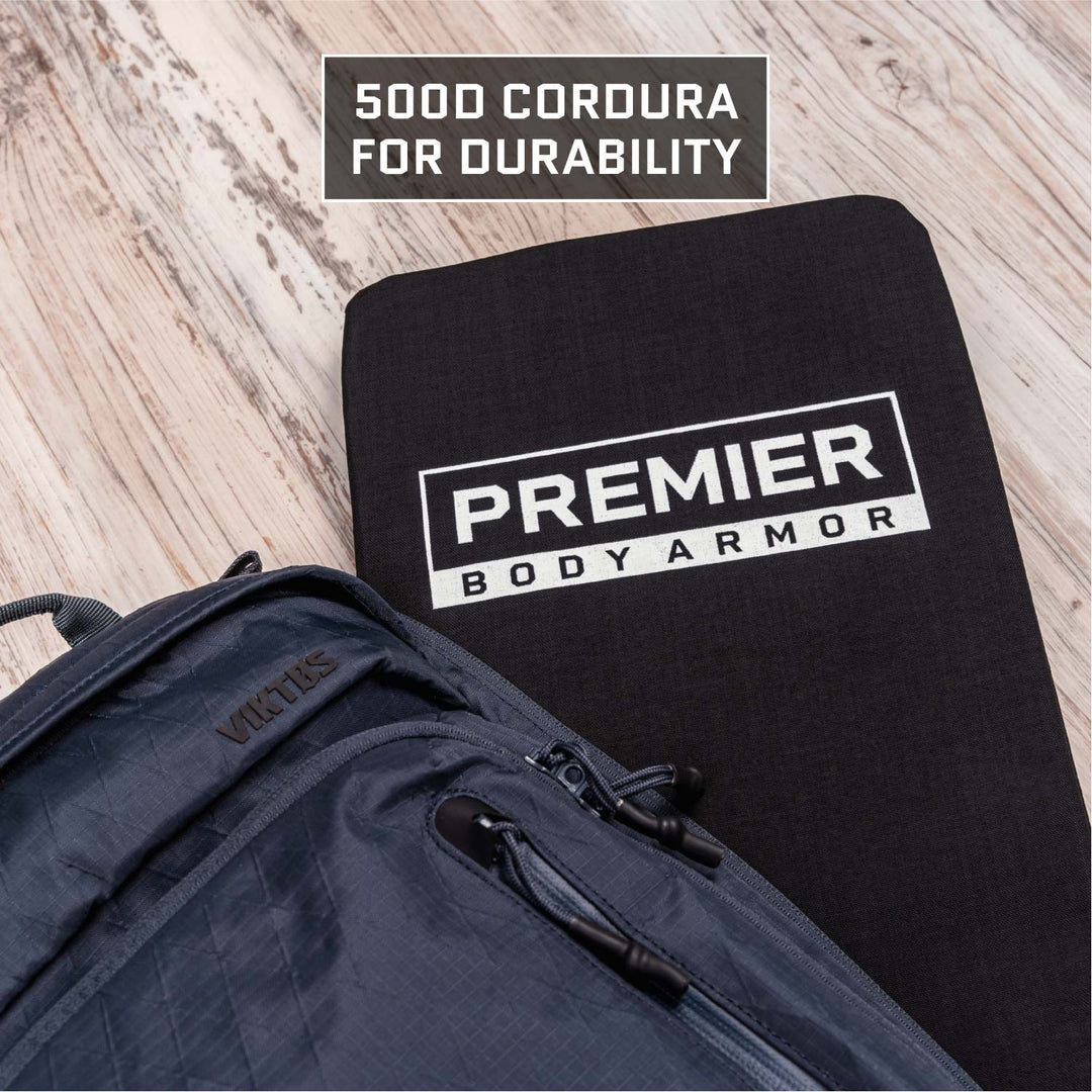 Close-up of a black "Premier Body Armor" panel next to a gray-textured backpack on light wood. A label highlights "500D Cordura for Durability," perfect for your tactical Armored Viktos Upscale Hip Pack Bundle or concealed carry essentials, by Viktos/Premier.