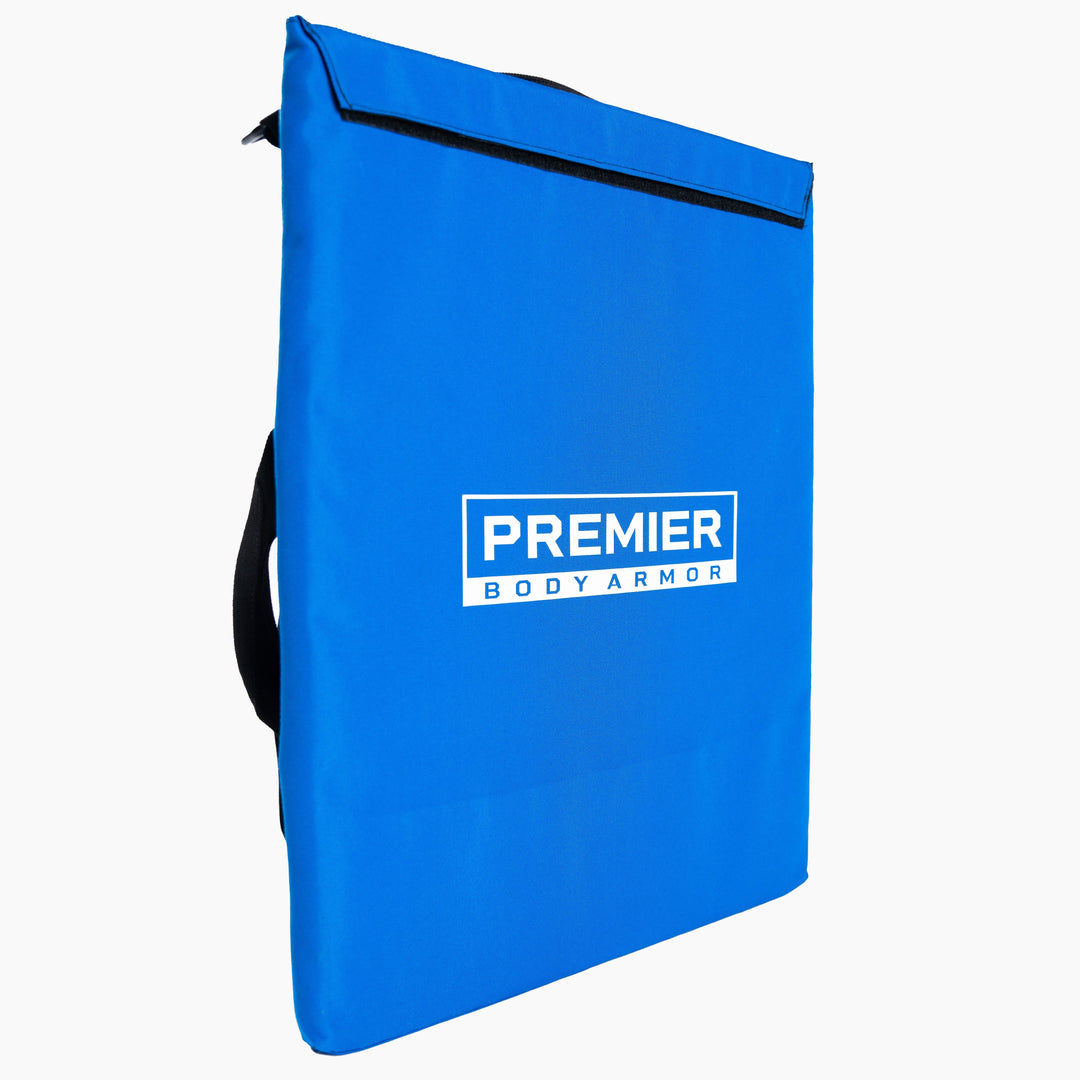 A blue rectangular bag with the text "Premier Body Armor" printed in white on the front. Equipped with black straps on one side and a black sealing strip near the top, this Level III+ First Aid Shield is perfect for enhancing school safety. The image features a plain white background.