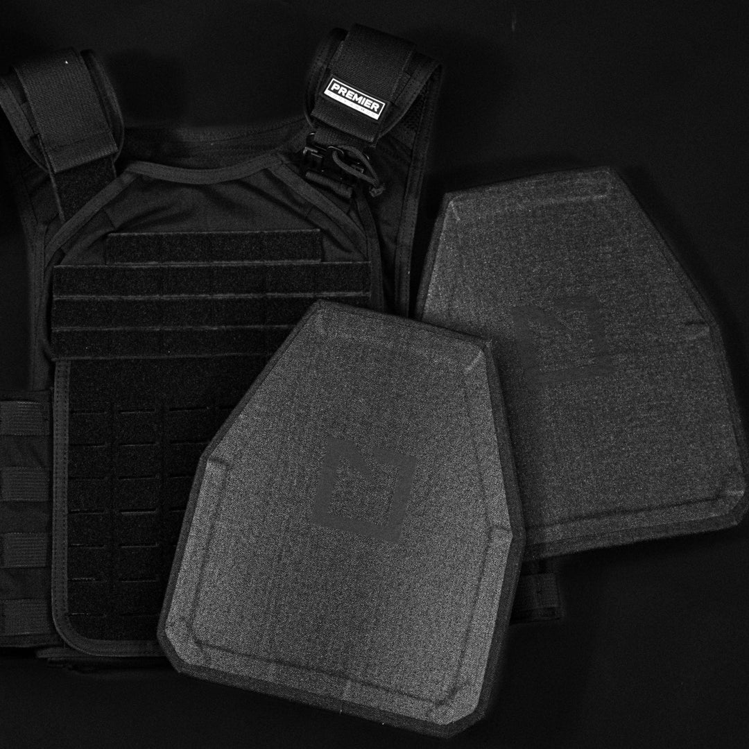 A black tactical plate carrier and Hesco L211 Special Threat Plate body armor, with ceramic/composite design, are displayed against a dark background. The adjustable carrier features straps and loops for perfect plate accommodation and enhanced protection.