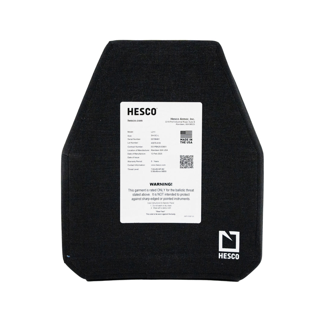 The image depicts a black HESCO L211 Special Threat Plate by Hesco, featuring a white label with branding, specs, warnings, and care instructions. This pentagon-shaped plate fits into vests and is a lightweight ceramic/composite design.