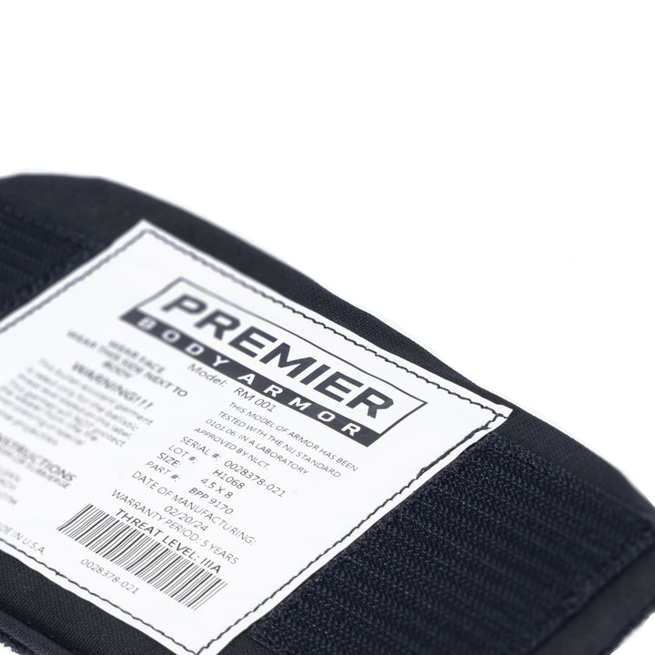 Close-up image of a Premier Body Armor label on a Vertx Everyday Fanny Pack Level IIIA Insert. The label contains product details such as the model (PM-01), date of manufacture, certification information, and warranty details. The ballistic panel is affixed to black fabric, suitable for use with the Vertx Everyday Fanny Pack.