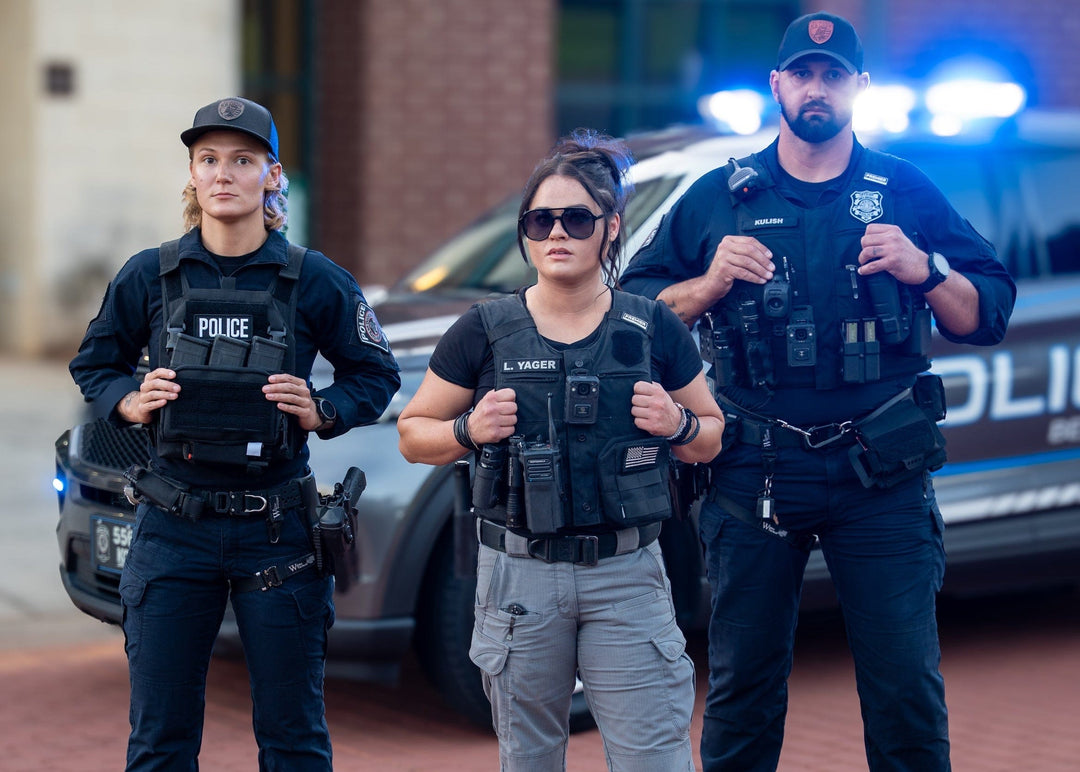 Three police officers standing on a brick pavement with a police vehicle in the background.