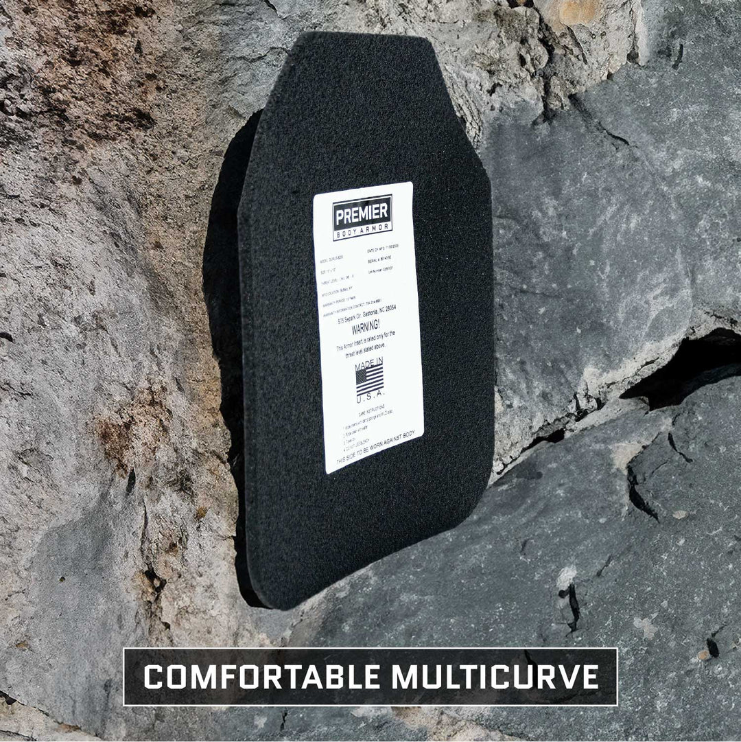 A black, multi-curve armor plate from Premier Body Armor is propped against a rock surface, showcasing the advanced ballistic protection features of the Durus 650 Level III+ Plate. The label displays product details and a barcode, with "Comfortable Multicurve" boldly printed at the bottom of the image.