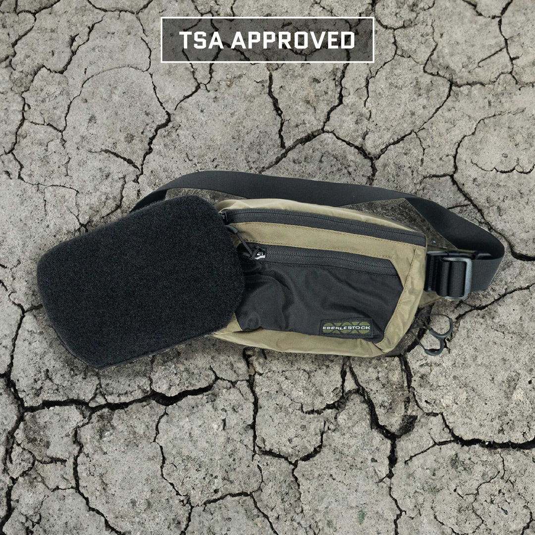 A beige and black Eberlestock Bando Bag featuring a black attachment sits on cracked earth. Above it, the text reads "TSA APPROVED," indicating its compliance with NIJ ballistic standards for increased safety while traveling. This bag includes the Premier Body Armor Level IIIA Insert for enhanced protection.