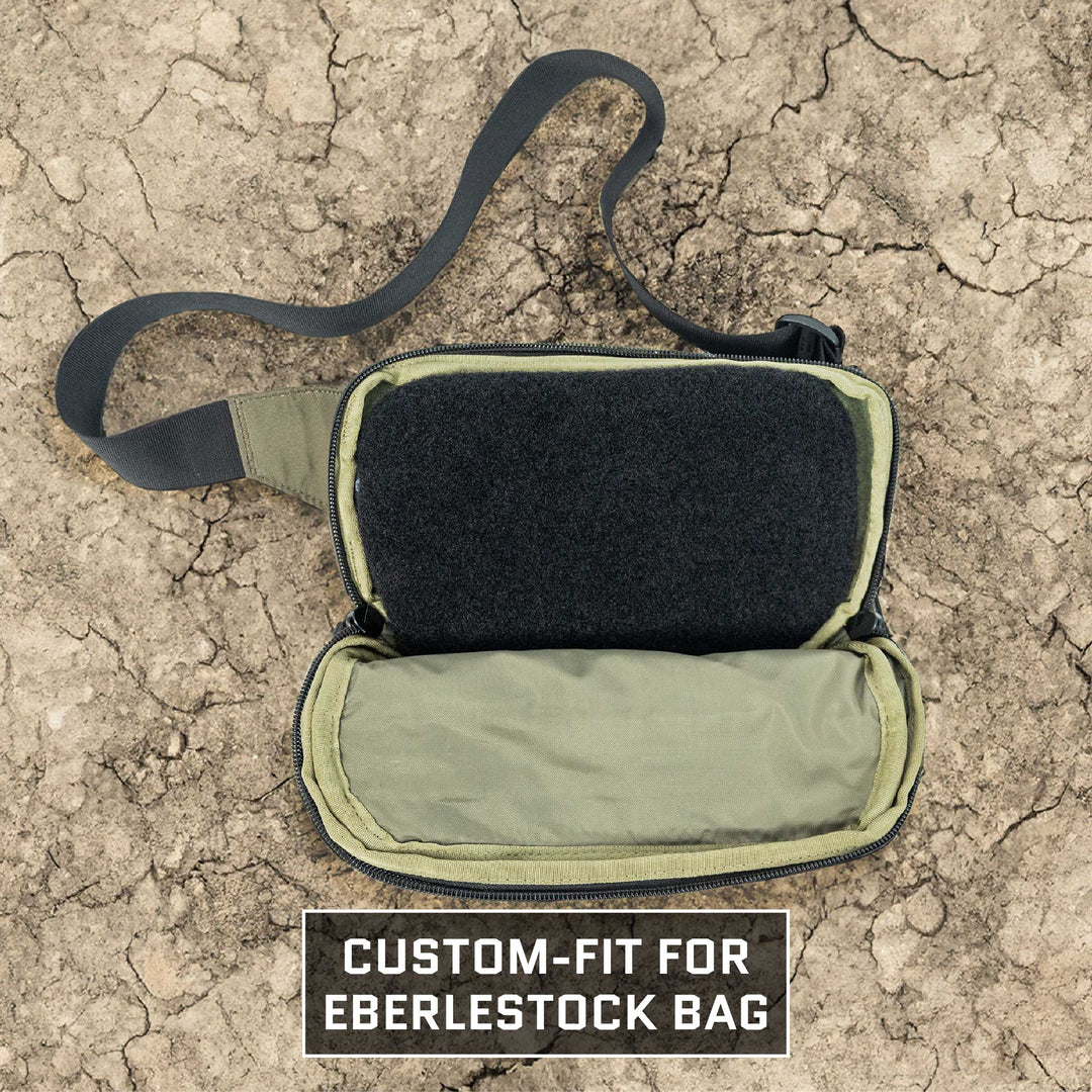 The dry, cracked ground serves as the backdrop for a Premier Body Armor Eberlestock Bando Bag Level IIIA Insert. This custom-fit accessory showcases its interior design with an open compartment and adheres to NIJ ballistic standards. Text at the bottom reads, "Custom-fit for Eberlestock bag.