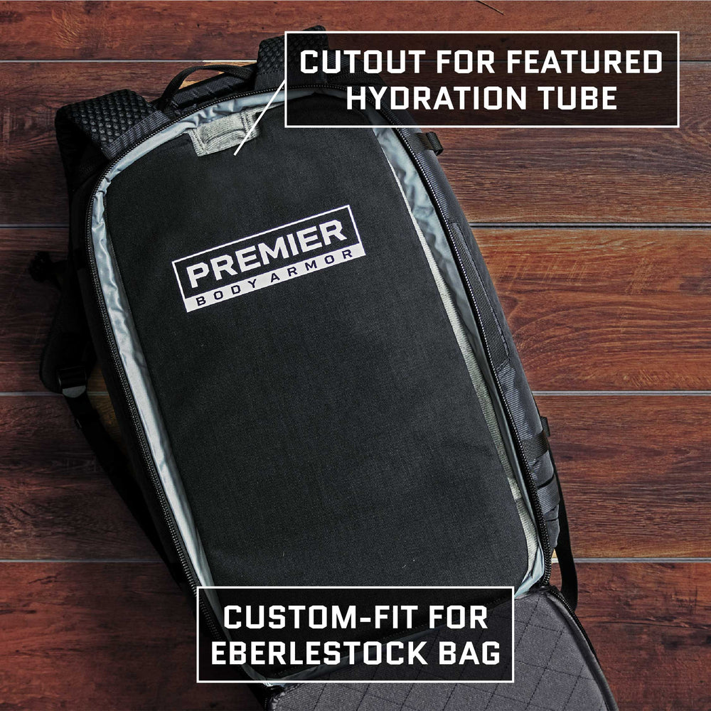 Displayed on a wooden floor, the Premier Body Armor Eberlestock Fade Adapt Level IIIA Insert fits perfectly within an Eberlestock Fade Adapt Backpack. It features a dedicated cutout for a hydration tube and is designed for custom integration, making it ideal for TSA-approved travel.