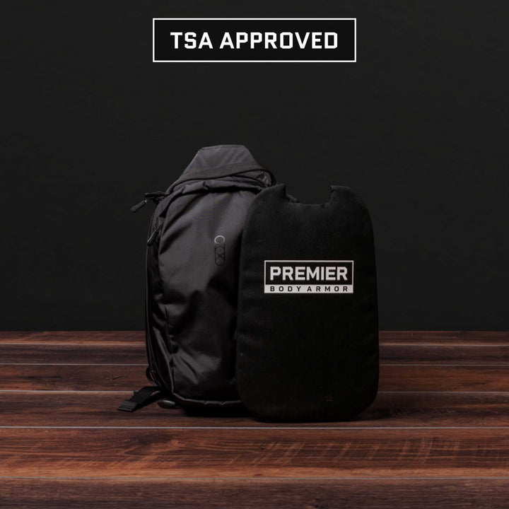 An Eberlestock Fade Sling Bag in black and a Level IIIA Insert labeled "Premier Body Armor" are placed on a wooden surface. Above them, the text "TSA Approved" stands out against a dark background.