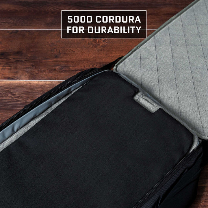 A close-up of an open backpack on a wooden surface shows a label reading "500D Cordura for durability." The inside fabric is quilted light gray, contrasting with the dark exterior. It's part of the TSA-approved collection featuring the Eberlestock Fade Transport 18 Level IIIA Insert by Premier Body Armor, renowned for its resilience.