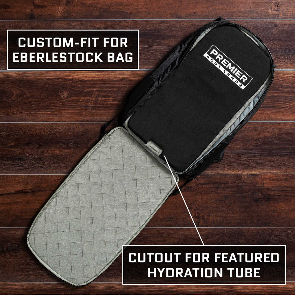 A black Eberlestock Fade Transport 18 Level IIIA Insert by Premier Body Armor, tailored to custom-fit the backpack, showcases a gray interior lining and includes a cutout for a hydration tube. Its sleek design is displayed on a dark wooden floor.