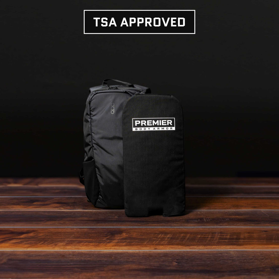 An Eberlestock Fade Transport 18 Level IIIA Insert and a rectangular black panel from Premier Body Armor rest elegantly on a wooden surface against a dark backdrop, with the comforting label "TSA Approved" prominently displayed above them.