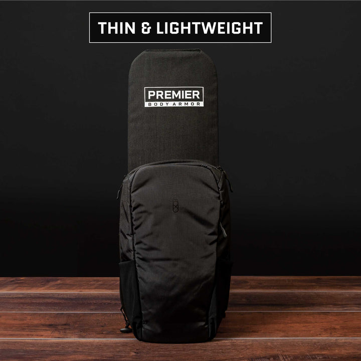 Set against a dark backdrop, an elegant and lightweight black backpack showcases the "Premier Body Armor" brand. The wooden floor beneath accentuates the contrast beautifully. This backpack is crafted for maximum protection, incorporating the Eberlestock Fade Transport 21 Level IIIA Insert to ensure added safety.