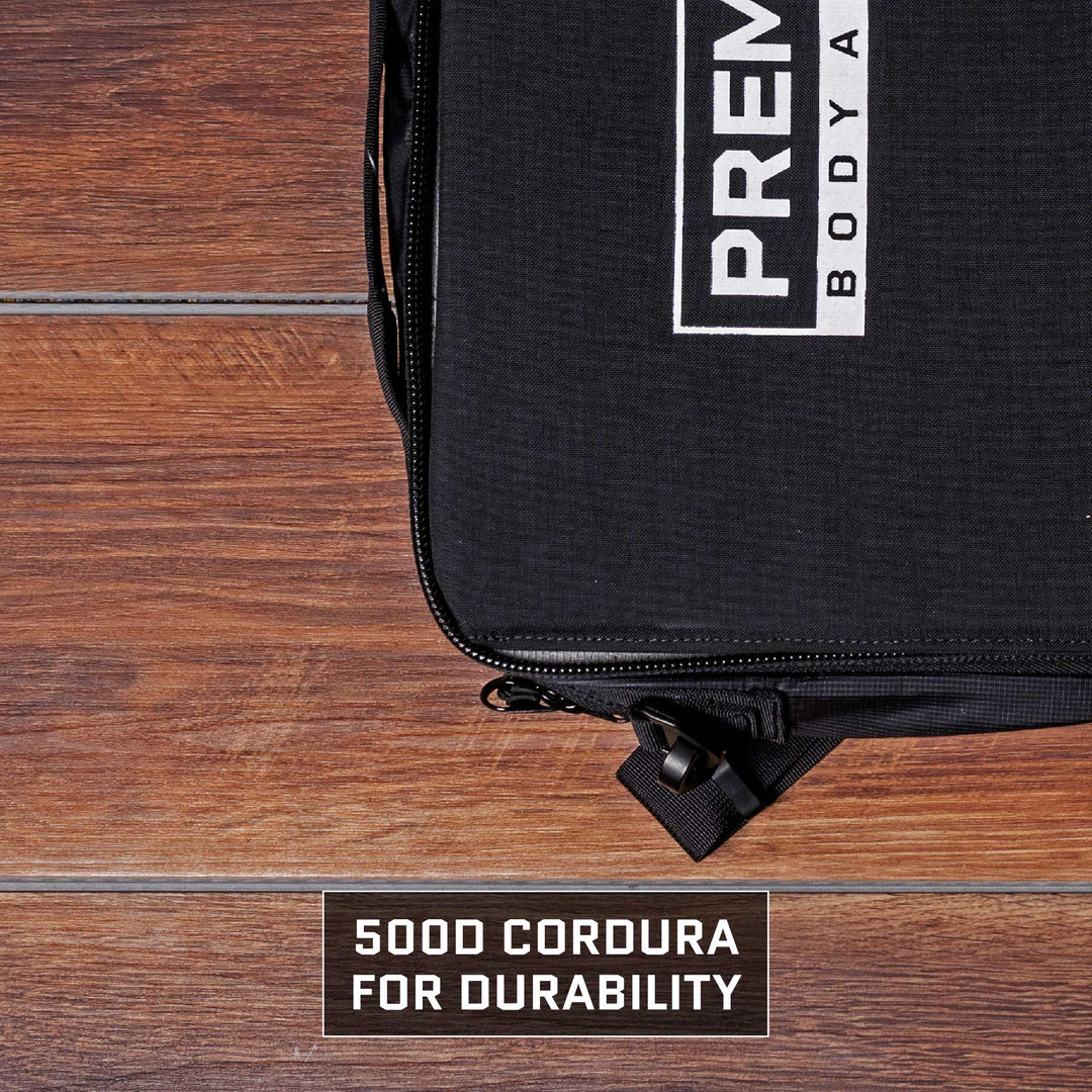 Close-up of a black Eberlestock Fade Brief Level IIIA Insert from Premier Body Armor with a visible zipper on a wooden surface. The bag showcases a partially visible white logo and text. Below, a label reads, "500D Cordura for Durability." This TSA Approved briefcase combines style with resilience for the modern traveler.
