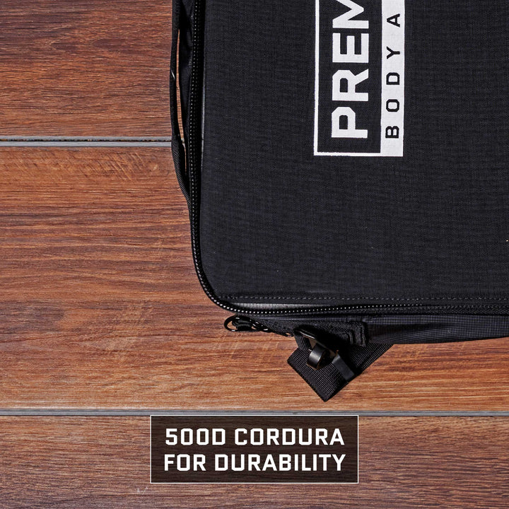 Close-up of a black Eberlestock Fade Brief Level IIIA Insert from Premier Body Armor with a visible zipper on a wooden surface. The bag showcases a partially visible white logo and text. Below, a label reads, "500D Cordura for Durability." This TSA Approved briefcase combines style with resilience for the modern traveler.
