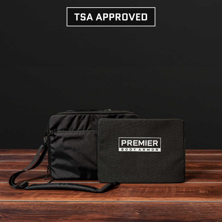 A black Eberlestock Fade Brief Level IIIA Insert by Premier Body Armor, complete with a shoulder strap, rests on a wooden surface against a dark backdrop. Adjacent to it is the Premier Level IIIA Body Armor panel. Above, the text prominently declares "TSA APPROVED," highlighting the seamless fusion of style and security.