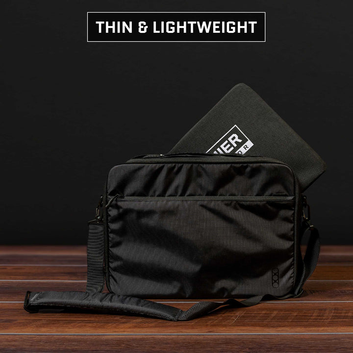 A sleek and lightweight black messenger bag, reminiscent of the design of a Premier Body Armor Fade Brief Level IIIA Insert, sits atop a wooden surface. Peeking out from inside is a black laptop sleeve with a rectangular label. The backdrop is black, and the text above reads "Thin & Lightweight.