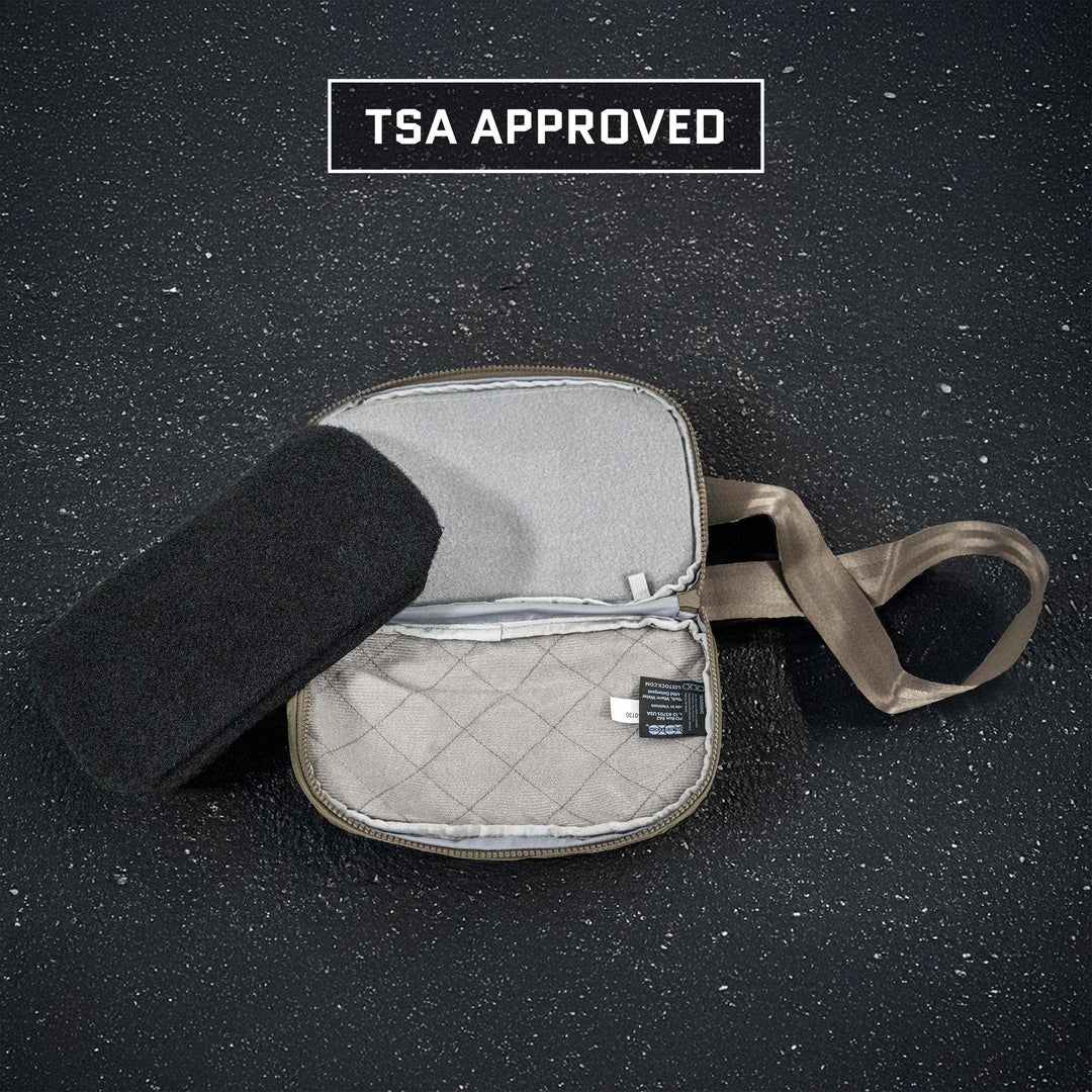 A small gray travel bag with a handle is open, revealing a quilted interior and a label. A black Eberlestock Fade Flex Level IIIA Insert by Premier Body Armor is on the left side. Above, "TSA Approved" text appears on a textured dark surface—ideal for safely storing your lightweight backpack armor.