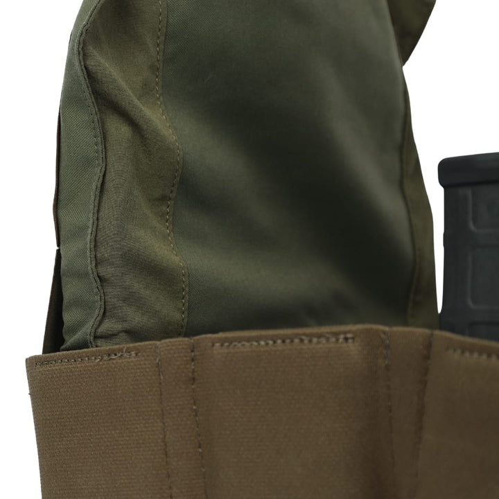A close-up of the Premier Body Armor Fortis Bravo Low Profile Carrier in green, featuring reinforced stitching and laser-cut MOLLE on brown fabric, with a black magazine partially visible on the right side.