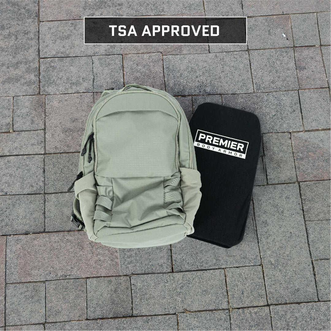 An Armored Vertx Ghost Pack Bundle from Vertx/Premier, featuring a light gray pack and a black armor plate, is displayed on a stone pavement. The phrase "TSA Approved" is prominently shown at the top of the image, emphasizing its attractiveness to tactical professionals in need of ballistic protection.